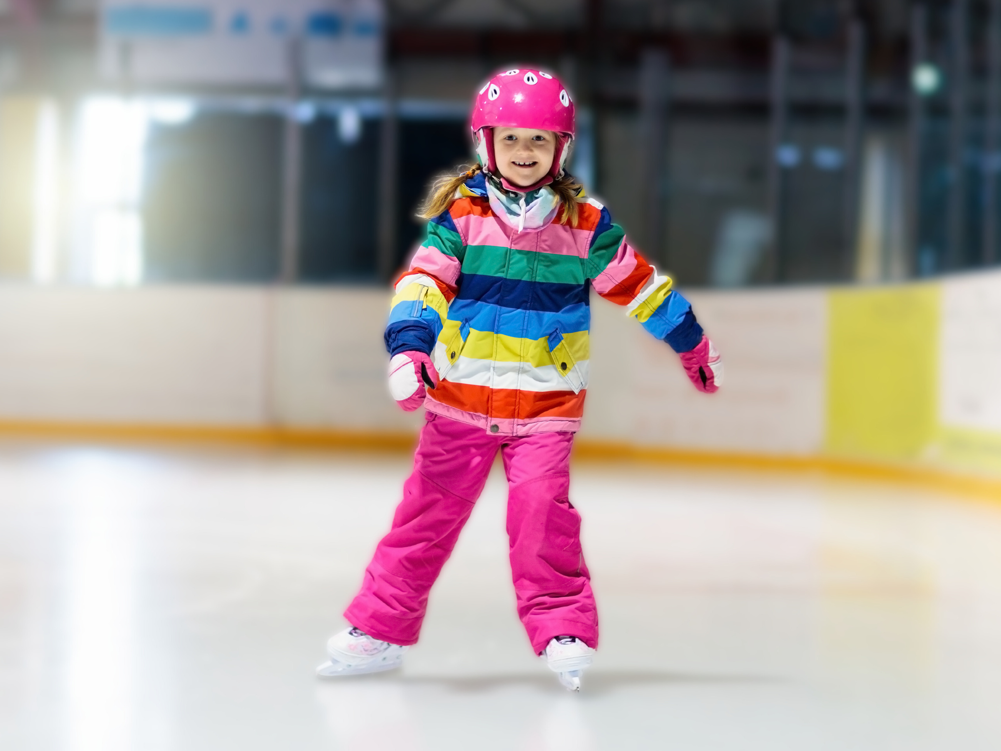 Kind in bunt gestreifter Winterkleidung und mit Helm läuft Schlittschuh