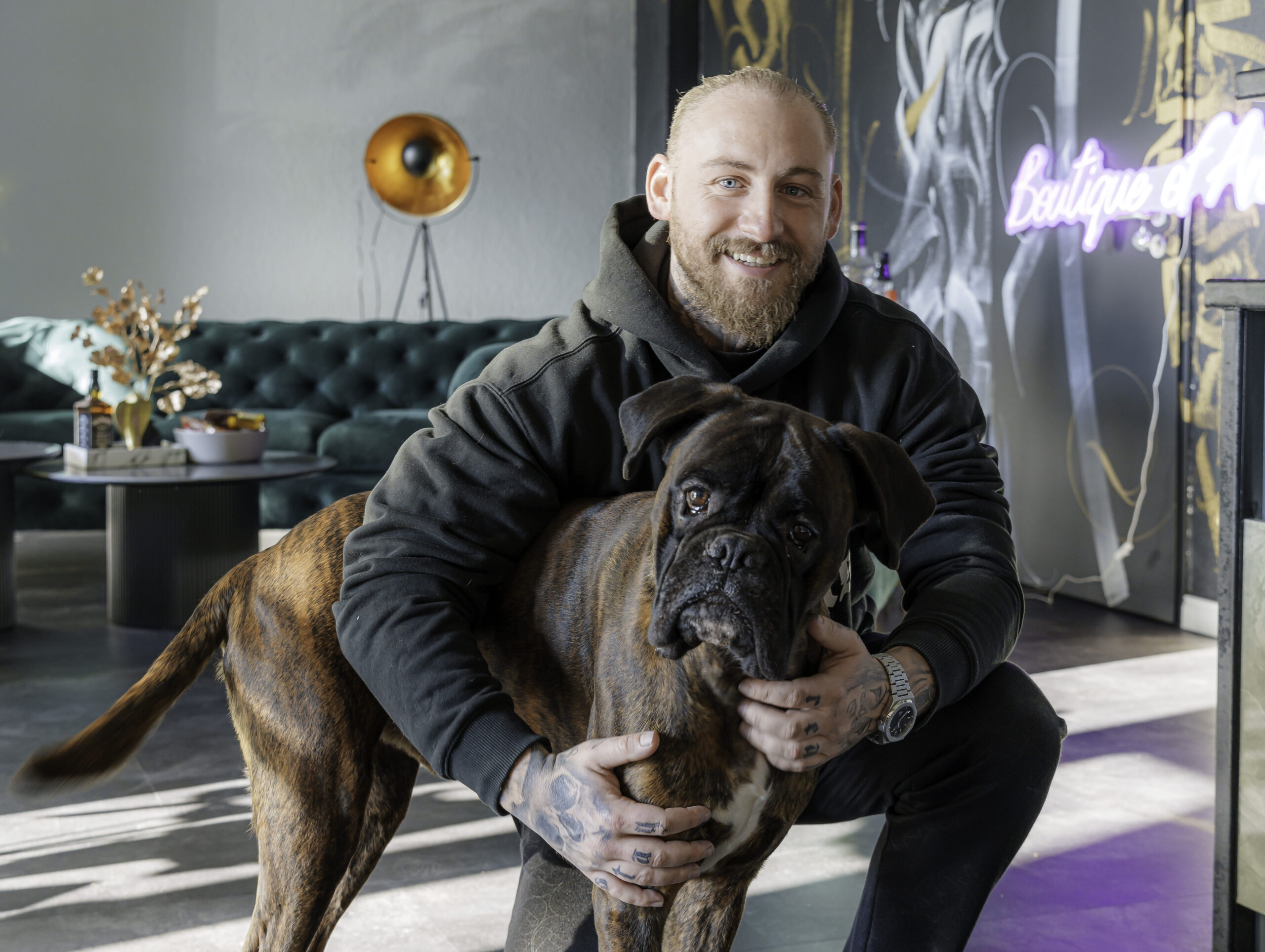 Rostocker Tätowierer Martin Jahncke kniet in seinem neuen Tattoo-Studio und umarmt seinen Boxer-Hund