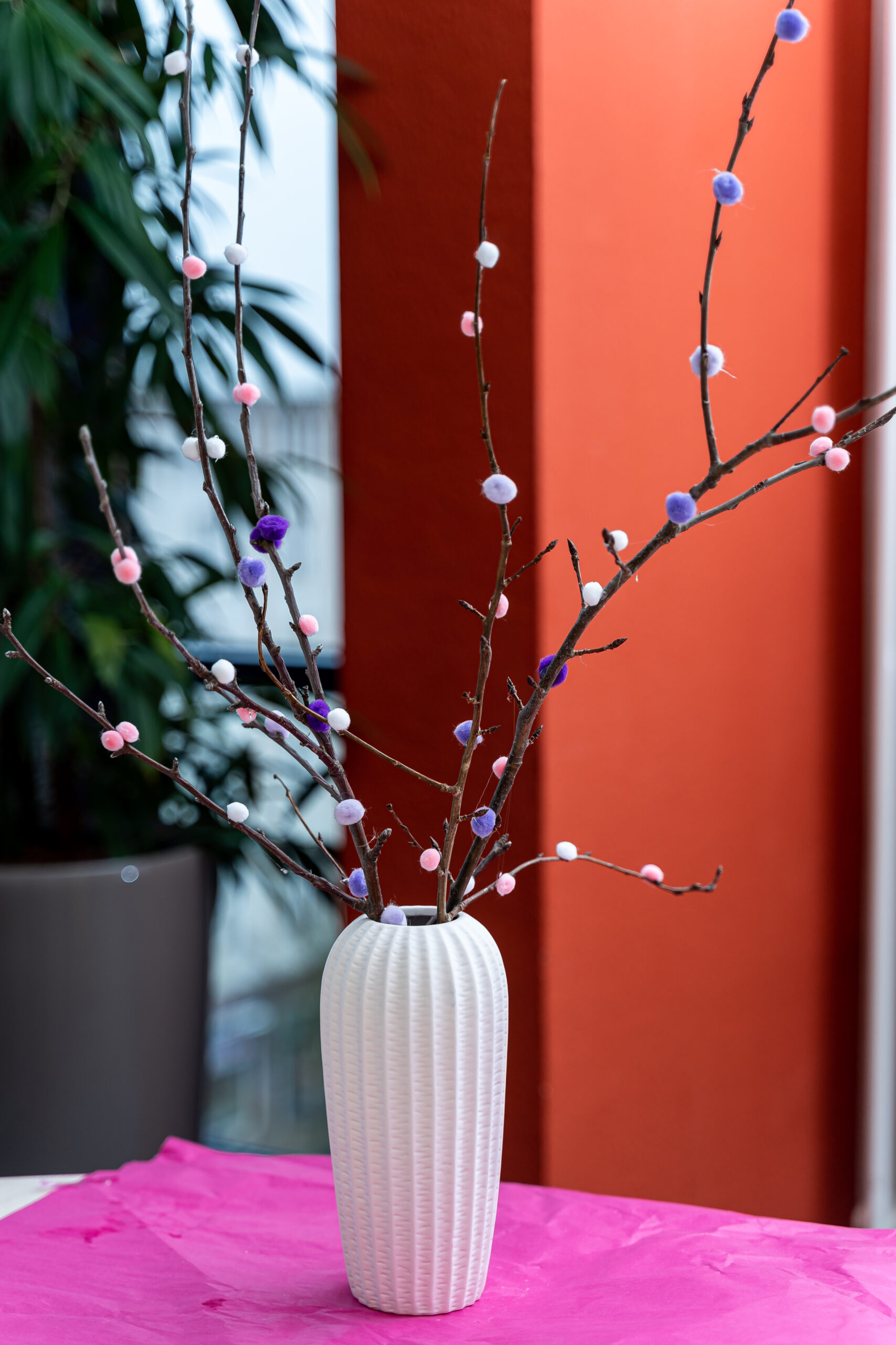 In einer weißen Vase stecken Zweige mit Pompom-Blüten in weiß, rosa und violett.