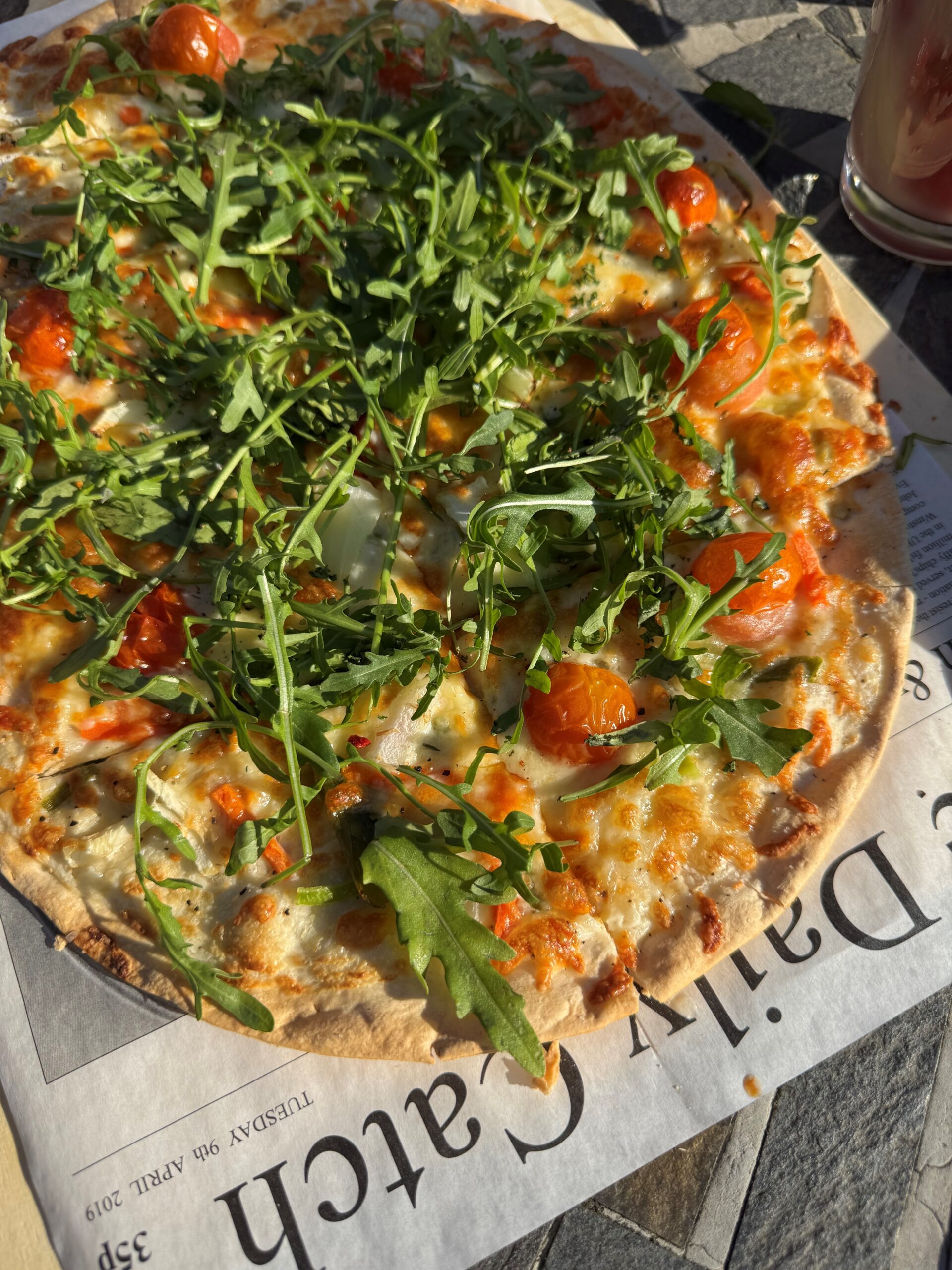 Flammkuchen vegetarisch DH Ein Flammkuchen mit Kirschtomaten, Rucola und Mozarella auf einer Zeitungsunterlage.