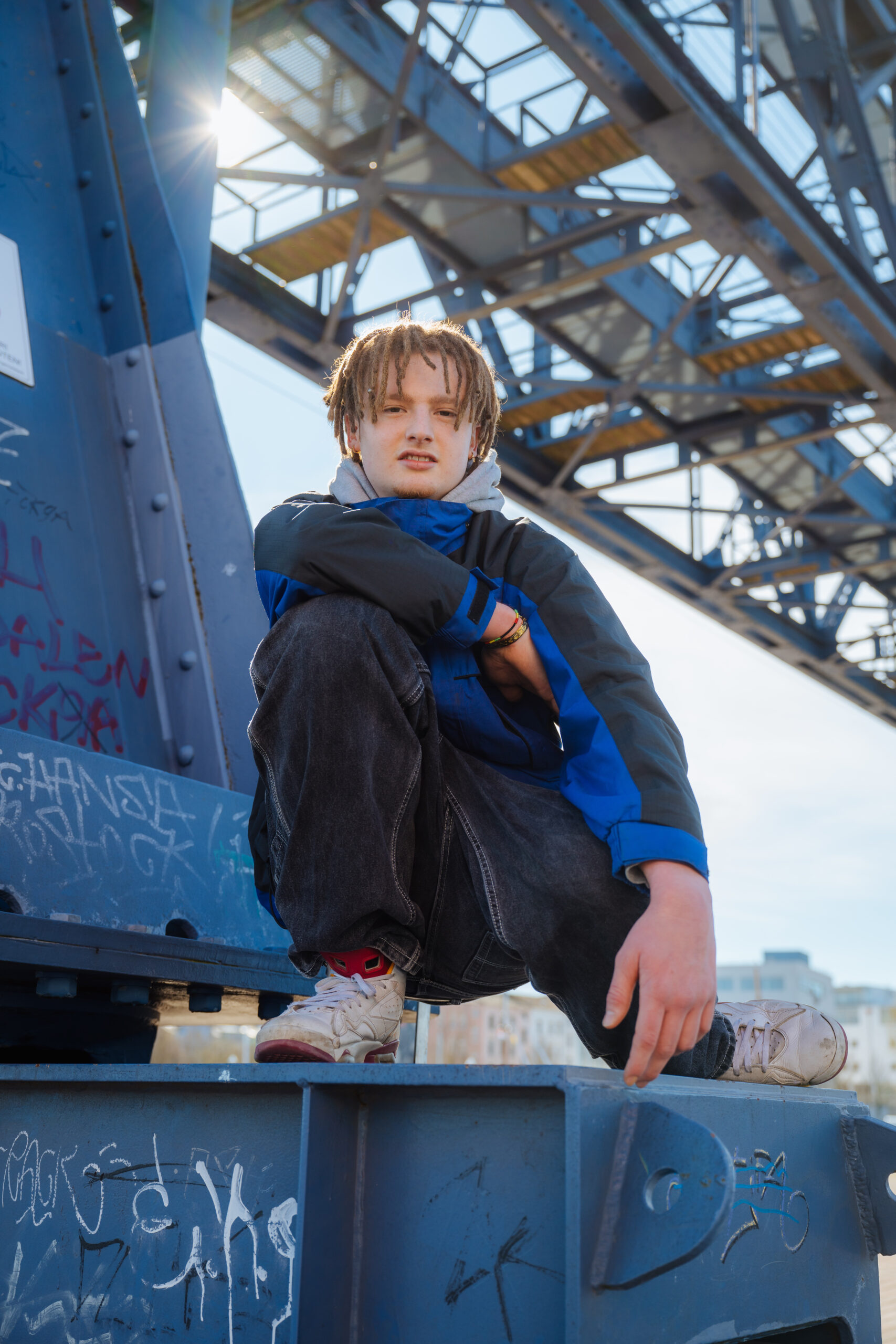Rapper Wicked Wanjo Nachwuchs-Rapper Wicked Wanjo posiert mit Rastazöpfen und Baggy-Jeans auf einem blauen Stahlkran.