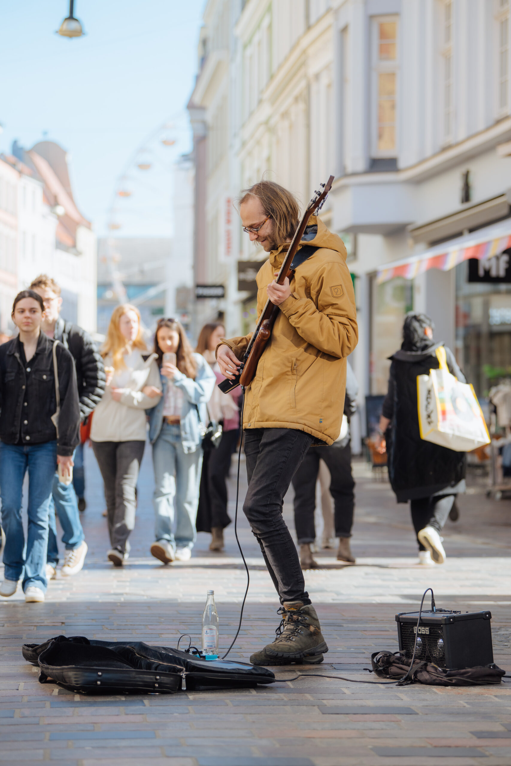 Straßenmusiker Henrik Plothe Straßenmusiker Henrik Plothe musiziert mit Gitarre in der Rostocker Kröpeliner Straße. Unübersehbar: sein gelber Parka und seine langen braunen Haare.
