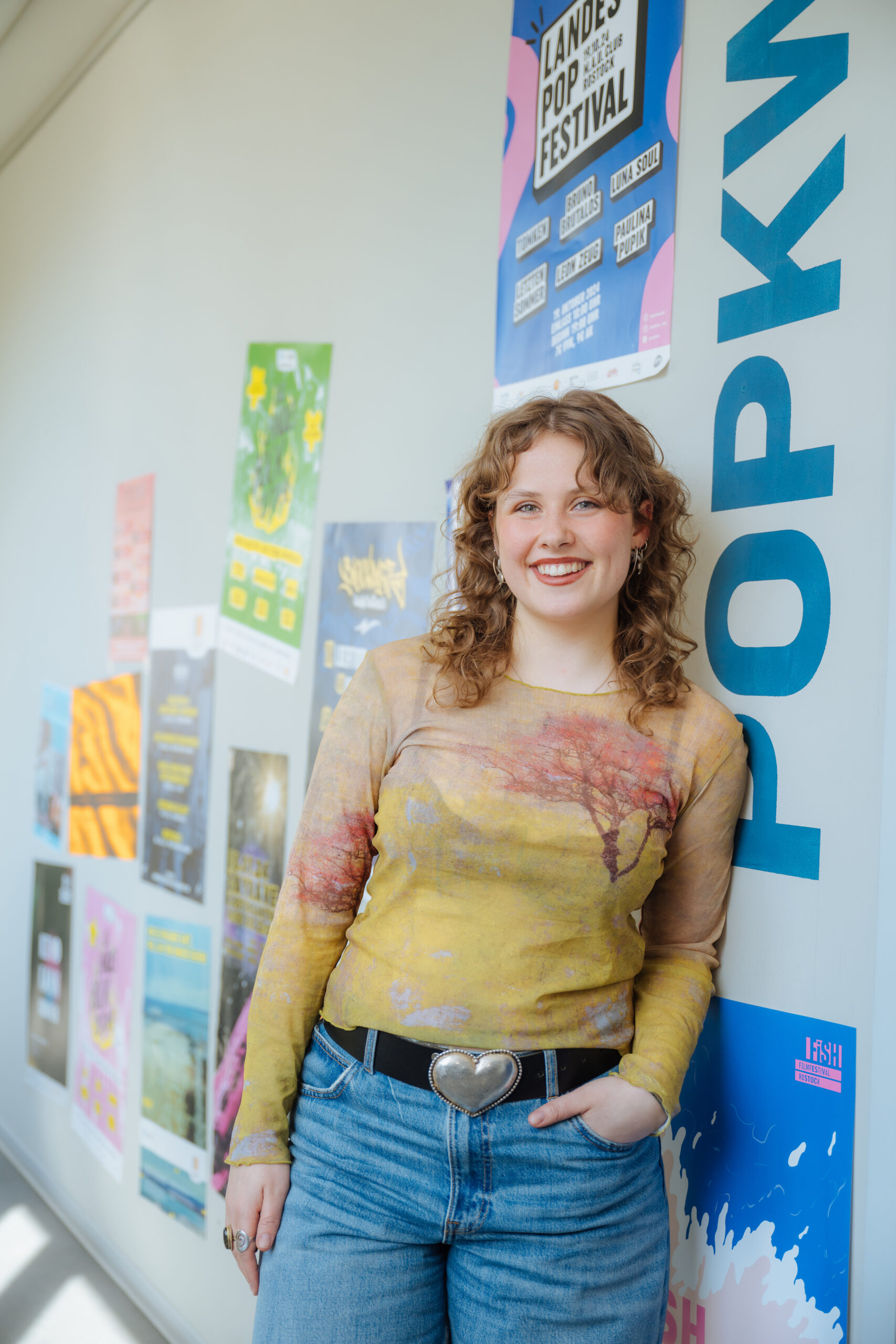 Martha Lea Hasselberg vom PopKW Martha Lea Hasselberg vom PopKW singt auch selbst, in der Band »Gelée« und im Duo »Marleo«. Sie steht locker vor einer bunt gestalteten Wand und trägt braune lockige Haare, ein gelbes Shirt und blaue Jeans.
