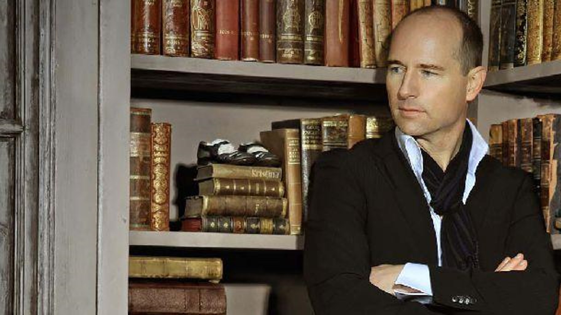 Olaf-Straube_Autor_intro Olaf Straube im schwarzen Anzug vor einem Bücherregal.