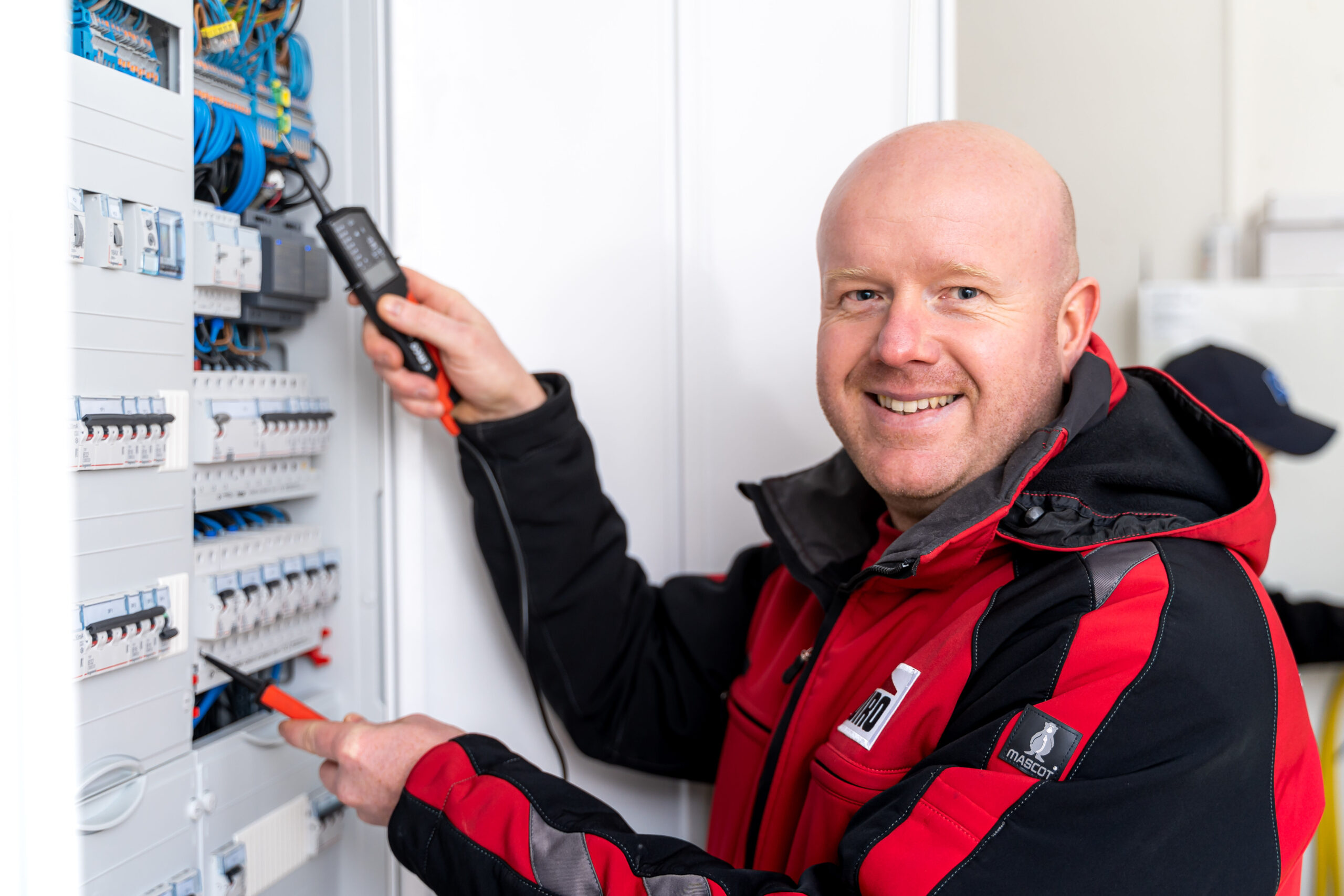 Der WIRO-Elektriker in rot-schwarzer Arbeitskleidung prüft die Sicherungen in einem Stromkasten.