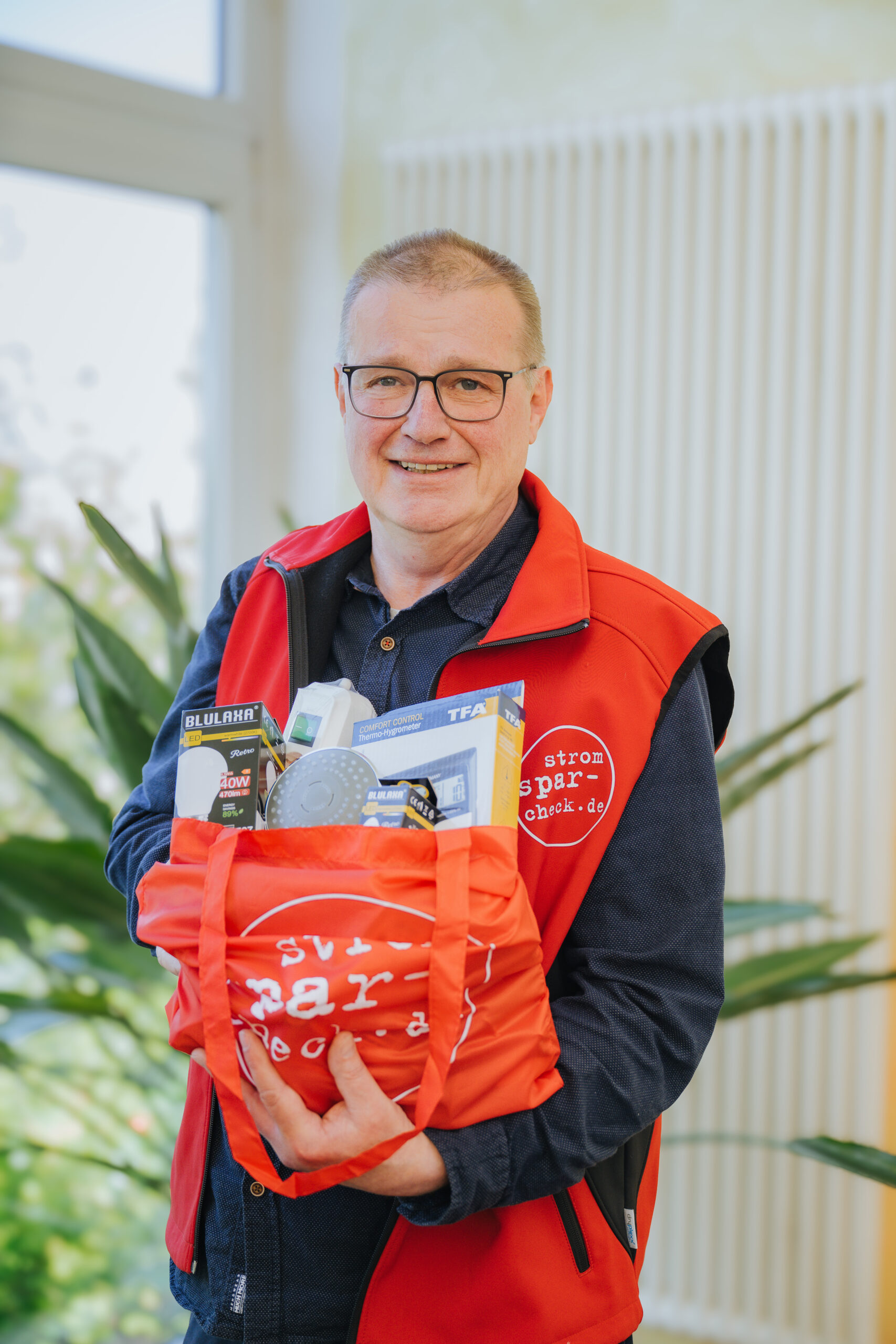 Stromsparcheck 2 York Kriesel, kurze Haare und Brille, vom AFW Rostock hält einen orangefarbenen Geschenke-Beutel in den Händen.