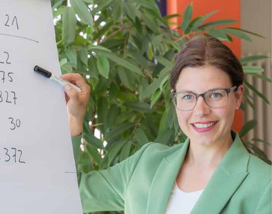 Laura Falk (brünett mit Brille) vor einem Flip-Chart mit Zahlen.