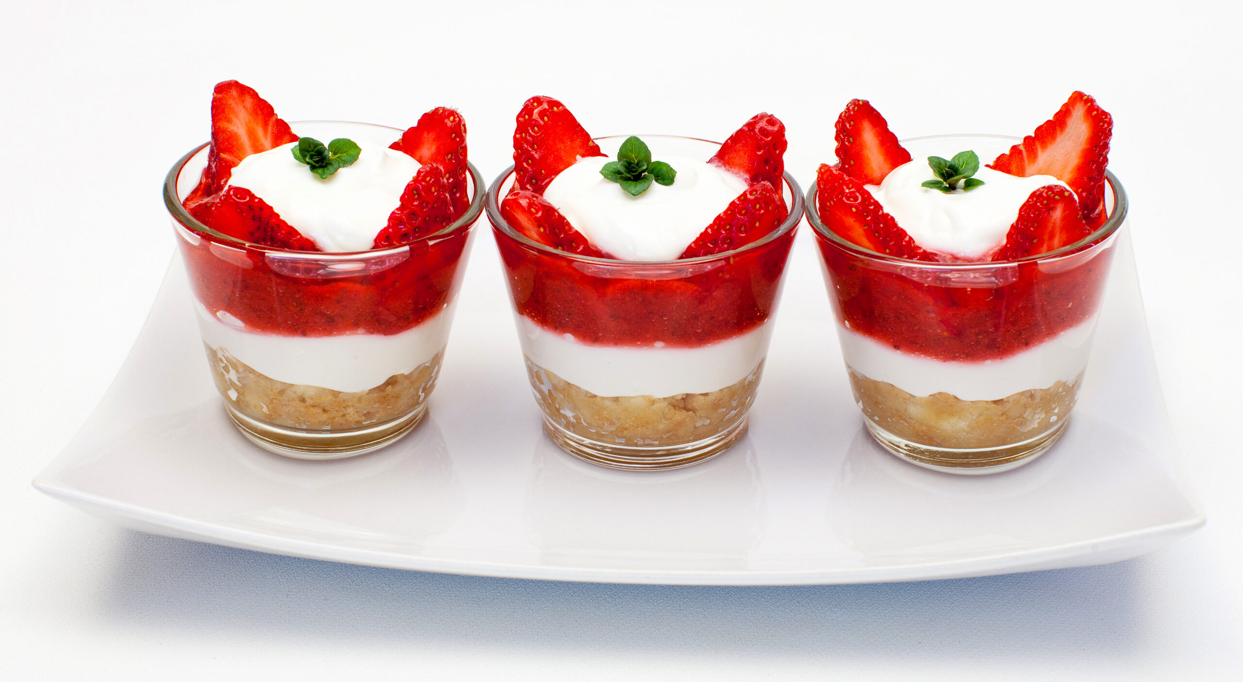 Erdbeer-Tiramisu 3 Gläschen mit köstlich aussehendem Erdbeer-Tiramisu auf einem weißen Teller.