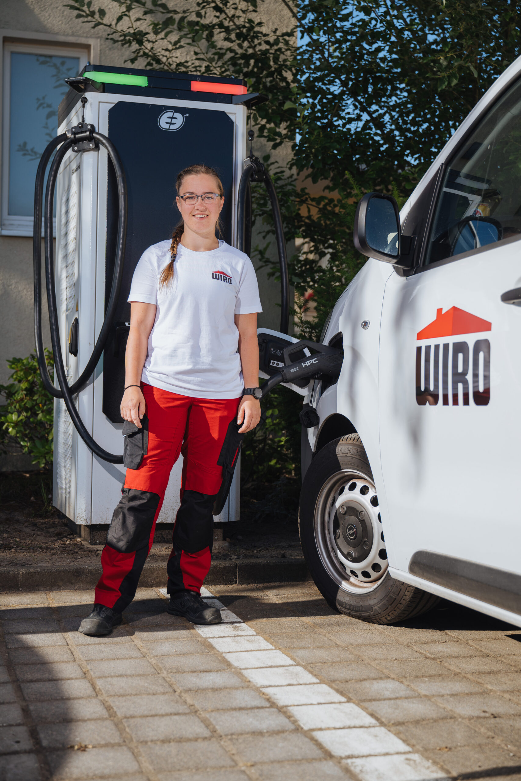 Stefanie Schneekloth Stefanie Schneekloth mit WIRO-Transporter an der E-Stromtankstelle. Die junge WIRO-Handwerkerin ist in weiß-roter Kleidung weithin zu erkennen.