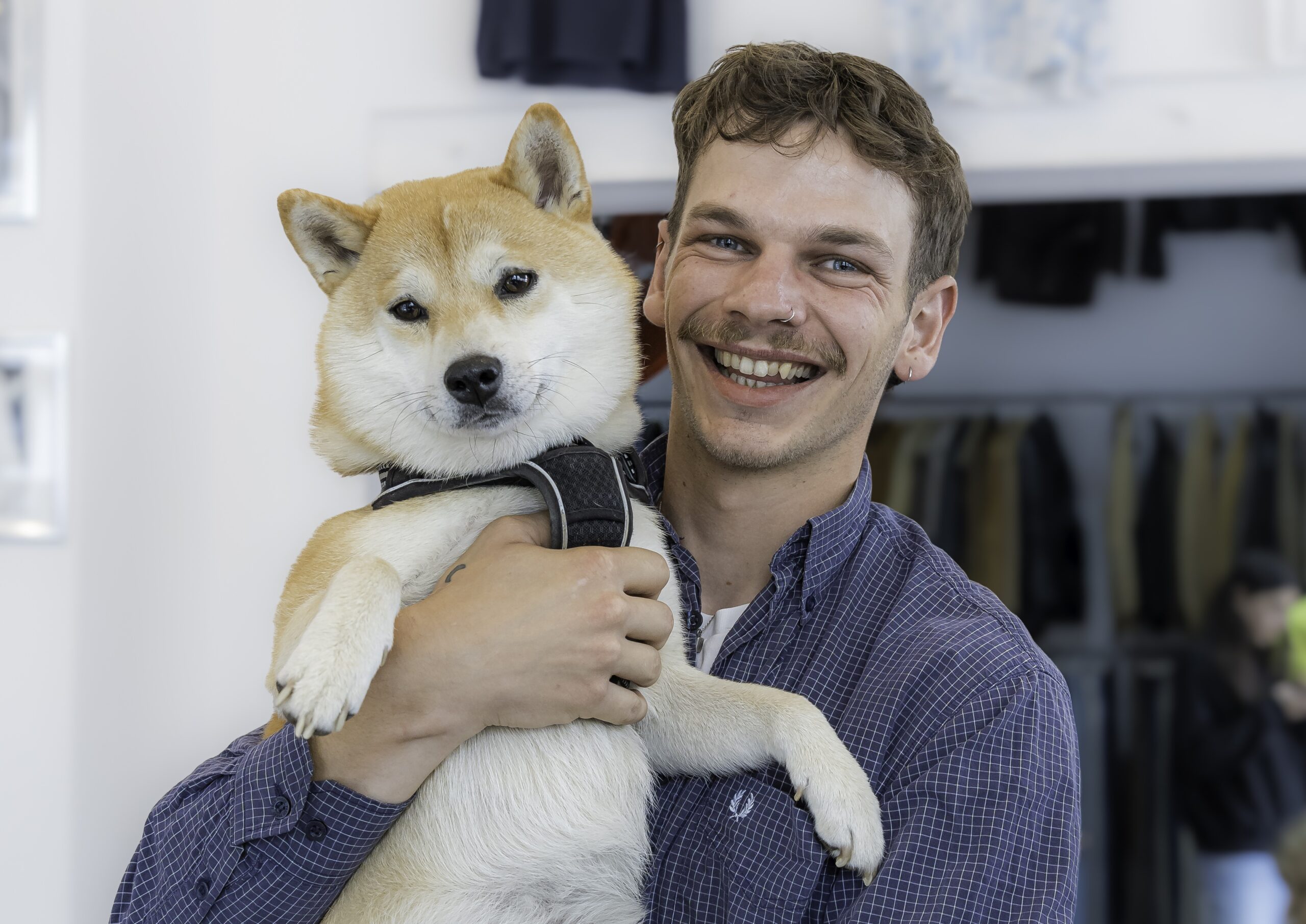 Maik Sprenger von MyVint im 90er-Look hält lachend seinen rot-weißen japanischen Hund im Arm.