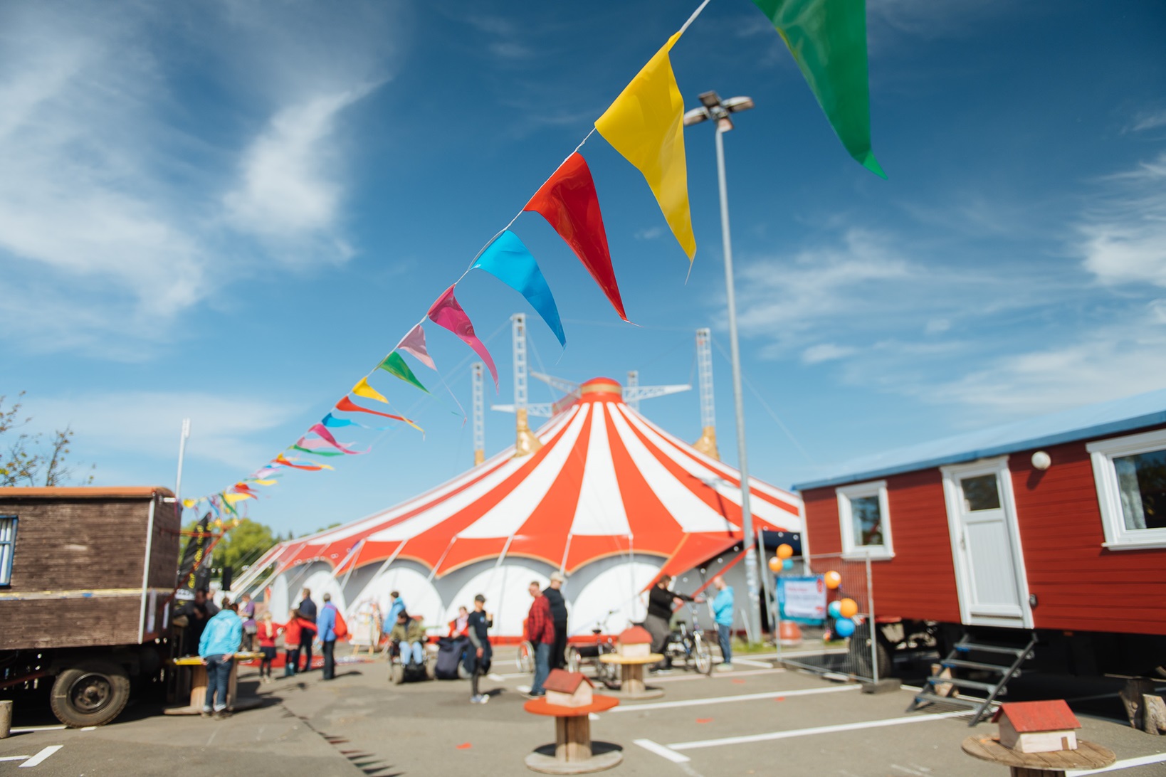 Sommerfest - Fantasia AG Sommerfest beim Circus Fantasia. Das orange-weiß gestreifte Zelt neben zwei Zirkuswagen. Bunte Wimpel wehen im Wind. Menschen unterhalten sich.