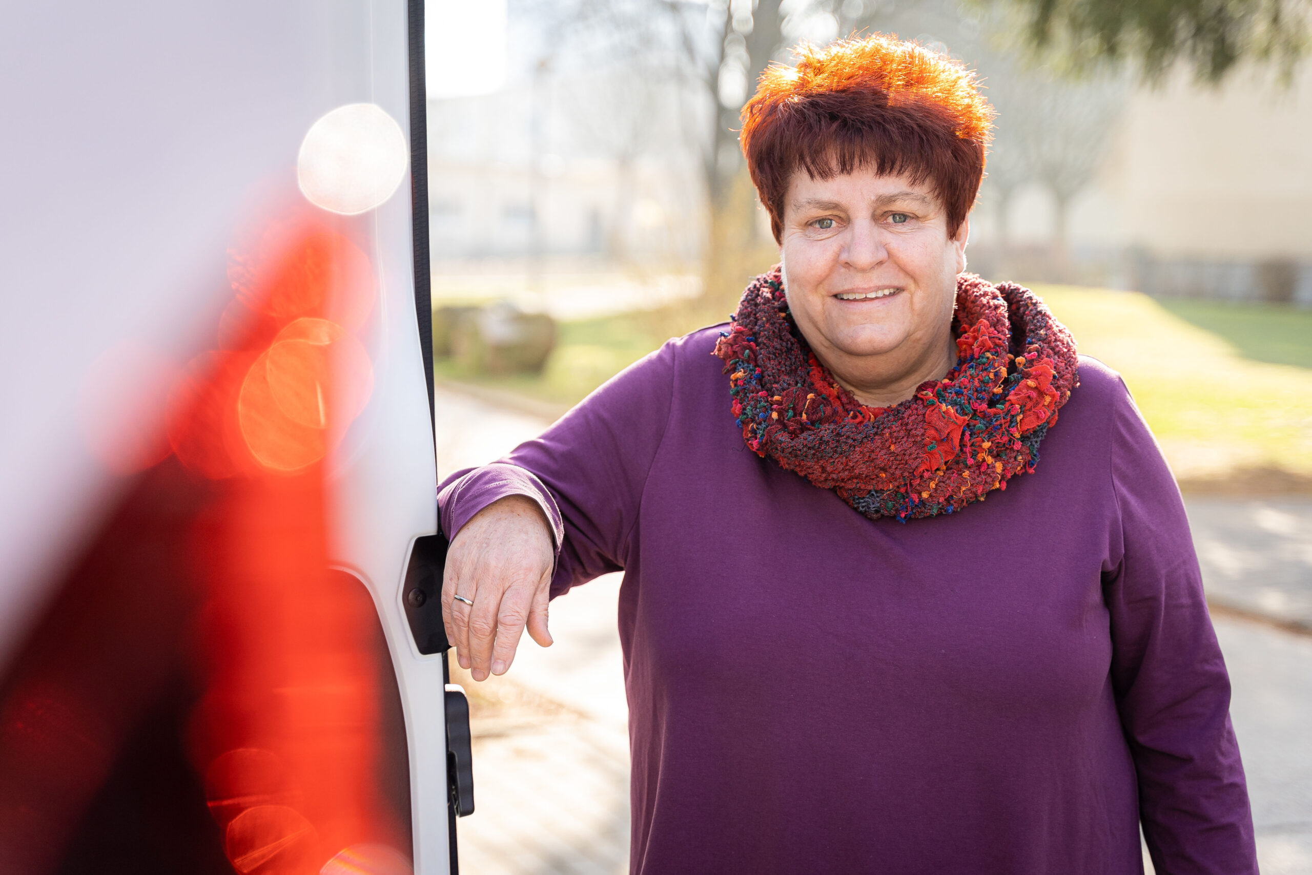 Babette Limp-Schelling, kurze rote Haare, rot-grün-gelber Schal und lila Pullover, an einem Transporter vom Wohltat e.V.