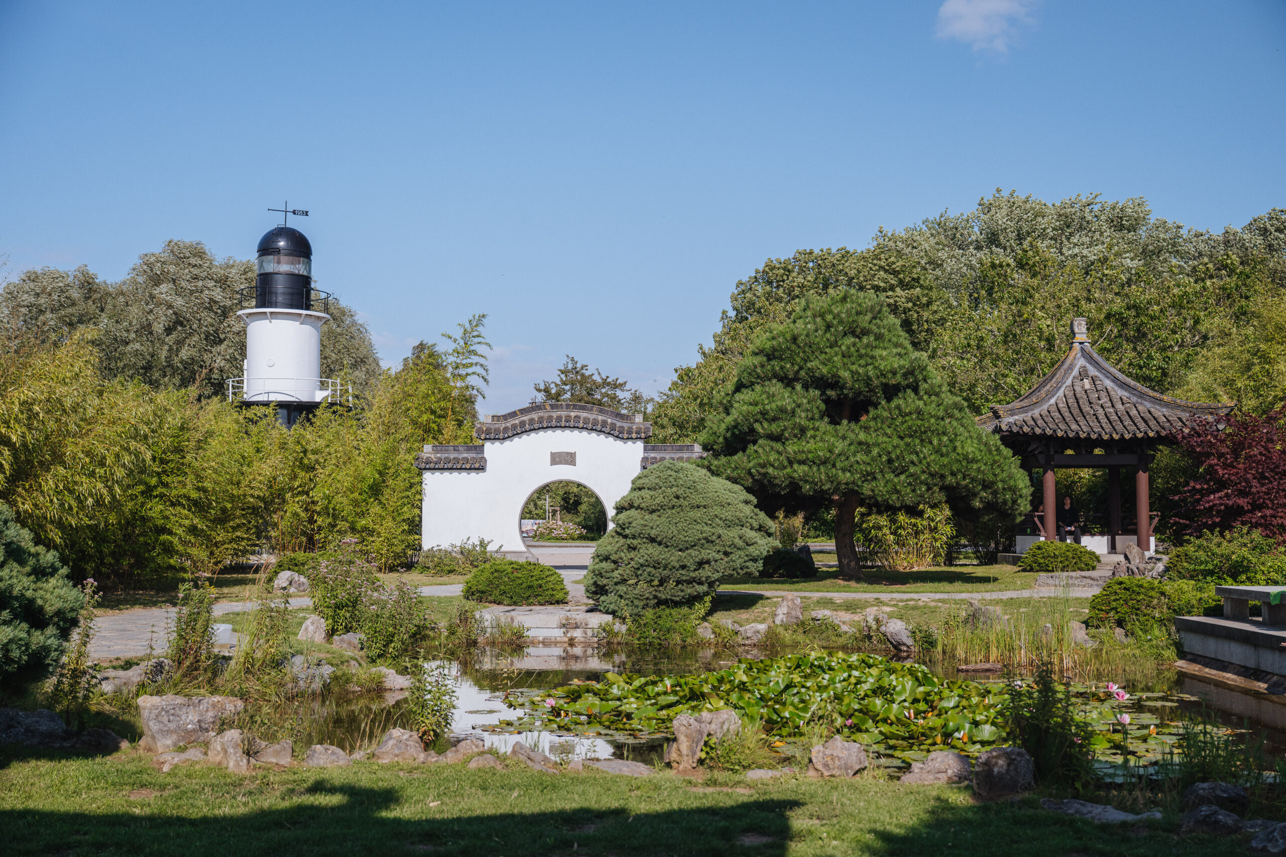 Chinesischer Garten in Rostocks IGA-Park mit Teich und schwimmenden Seerosen. Im Hintergrund typisch chinesische Architektur mit einem Pavillon (Ting) und einem Tor (Paifang oder Pailou).
