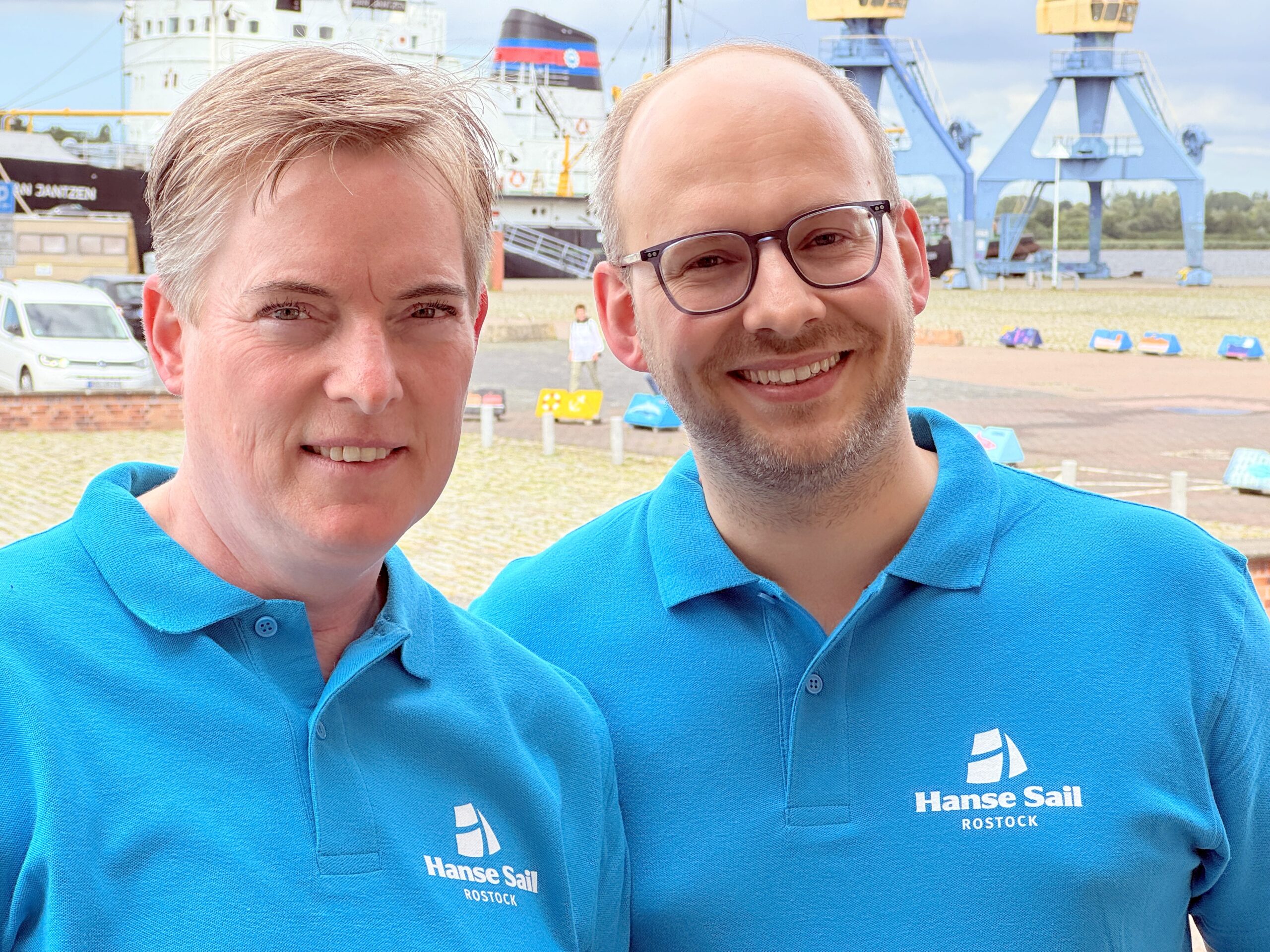 Angela Dankers und Thomas Gorny in hellblauen Polo-Hemden vom Hanse Sail Verein lächeln in die Kamera.