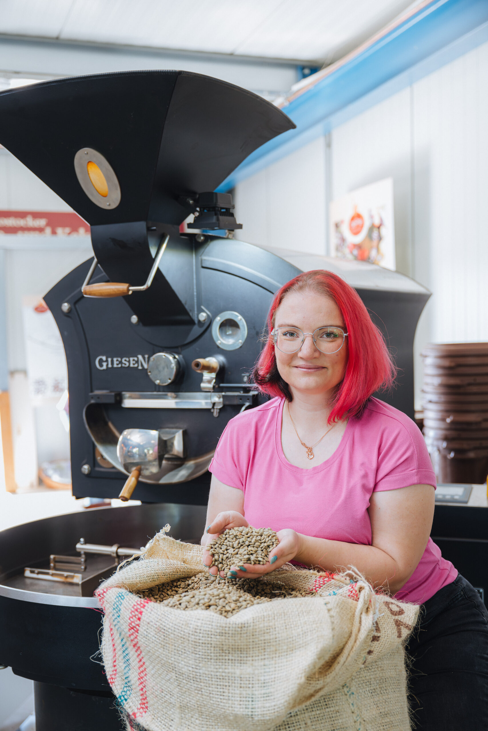 Kristine Rönnpagel von der »Schokoladerie de Prie« im Schmarler Fährhaus schöpft mit den Händen rohe Kaffeebohnen aus einem großen Kaffeesack. Sie steht neben einer großen Röstmaschine.