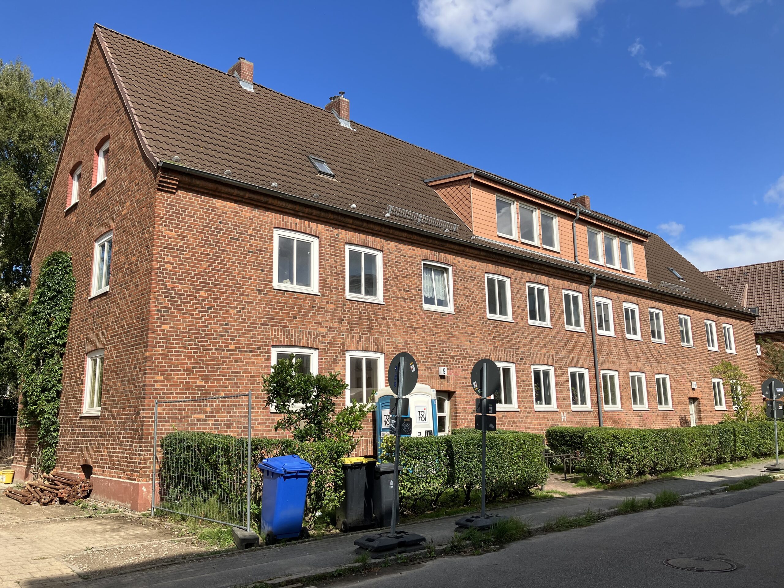 Ein unsaniertes WIRO-Mehrfamilien-Backsteinhaus in der Warnemünder Lortzingstraße 9 - 10. Gesäumt wird das Haus von einer grünen Hecke.