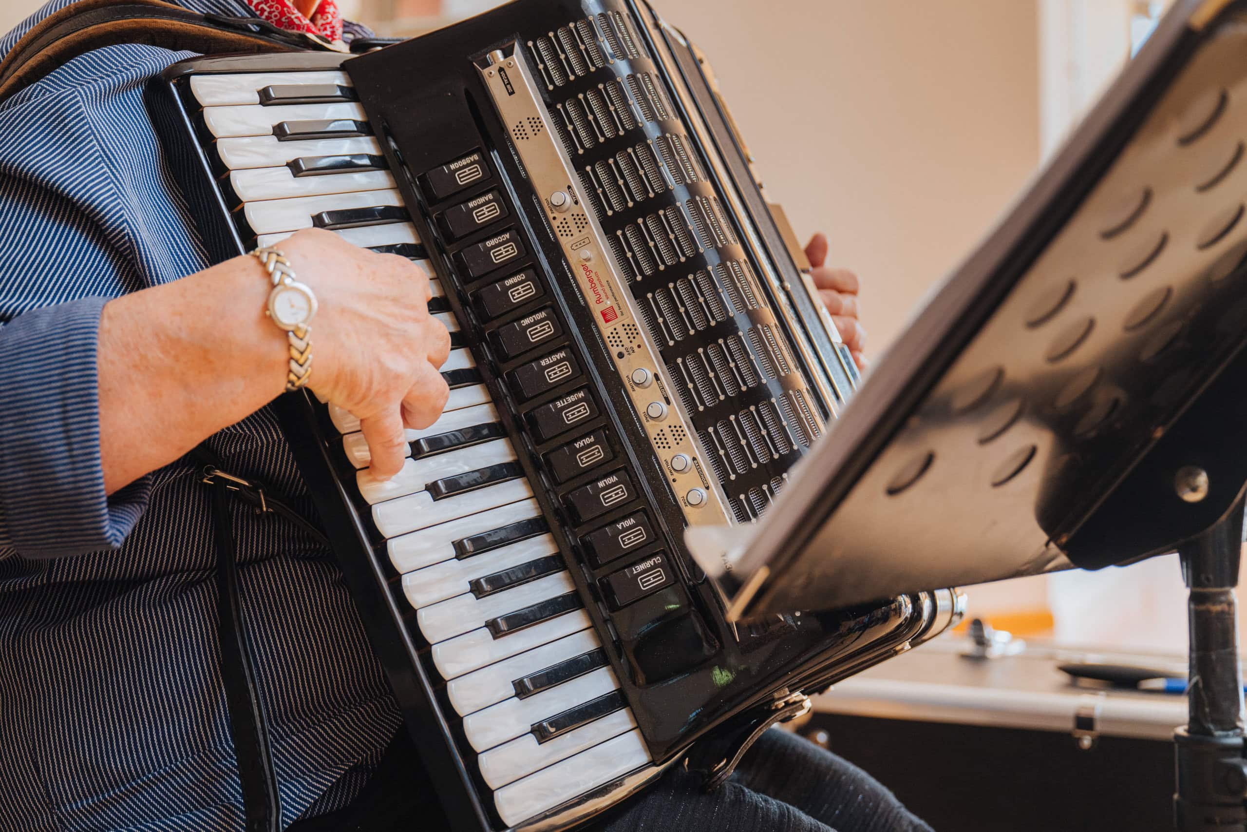 Die Hand einer Dame bespielt die schwarz-weiße Tastatur eines schwarz-goldenen Akkordeons, das in Großaufnahme zu sehen ist.