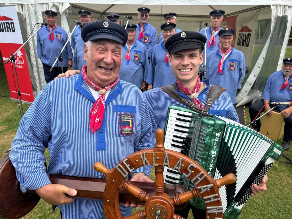 Klaashahns Fotos mit Günther Hamann und Max Nadzeika Günther Hamann (links), Vereinsvorsitzender, und Chorleiter der Klaashahns, Max Nadzeika, in blau-weiß gestreiften Matrosenhemden mit einem Steuerrad und einem Akkordeon vor dem Chor.