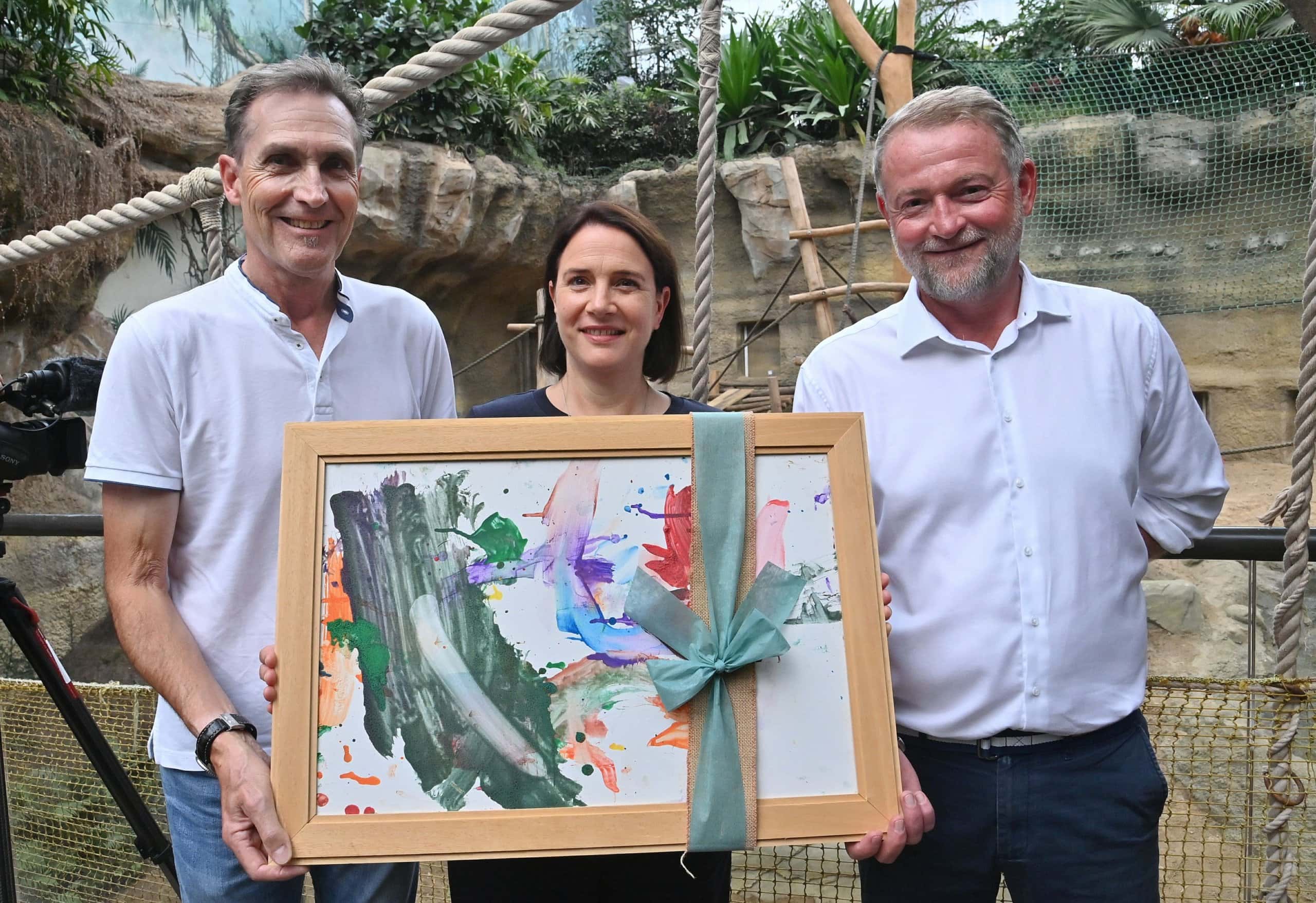 Ralf Zimlich, WIRO-Chef, Antje Angeli, Zoodirektorin, und Ingo Hübner, operativer Geschäftsführer der WIRO, bei der Eröffnung des neuen Orang-Utan-Geheges 2025 mit einem großen bunten Bild in den Händen.