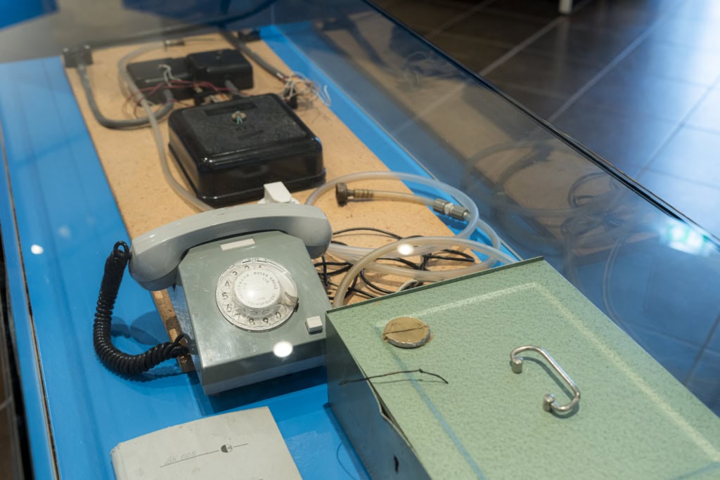 Neben einer alten Geldkassette steht ein graues DDR-Telefon mit Abhör-Equipment, das die Stasi zu DDR-Zeiten nutzte, um Bürger auszuspionieren.