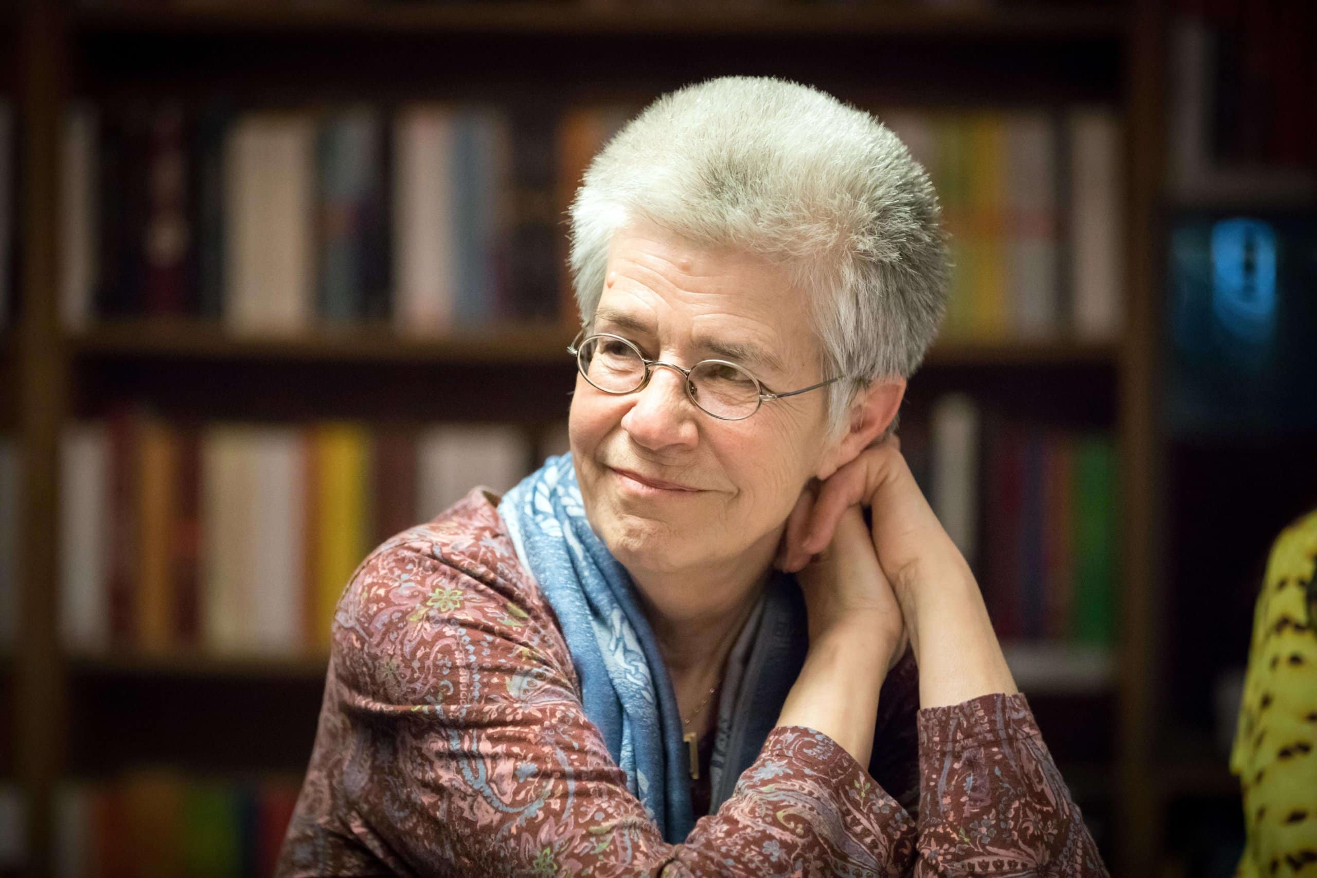Elke Schilling, graue Haare, Brille, sitzt lächelnd vor einem Bücherregal, und ist die Gründerin des Silbernetz e. V., bei dem ältere Menschen aus ganz Deutschland ein offenes Ohr finden.