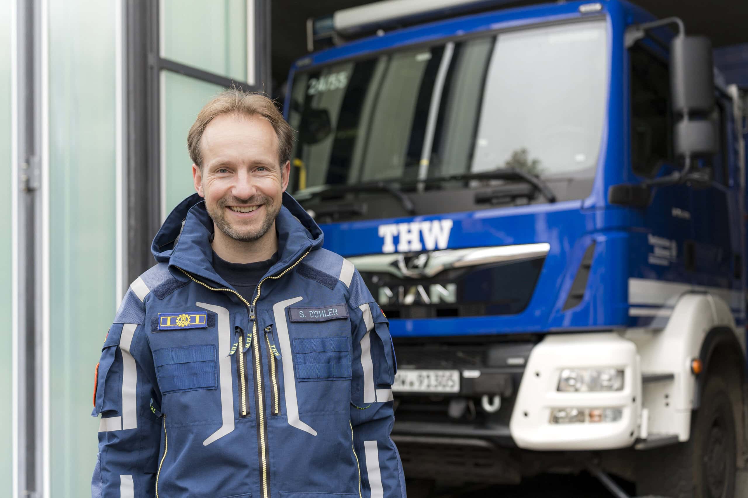 Stephan Döhler in der blauen Kluft des THW vor einem großen Einsatzfahrzeug rät, sich eine Lebensmittelreserve für die Not anzulegen.