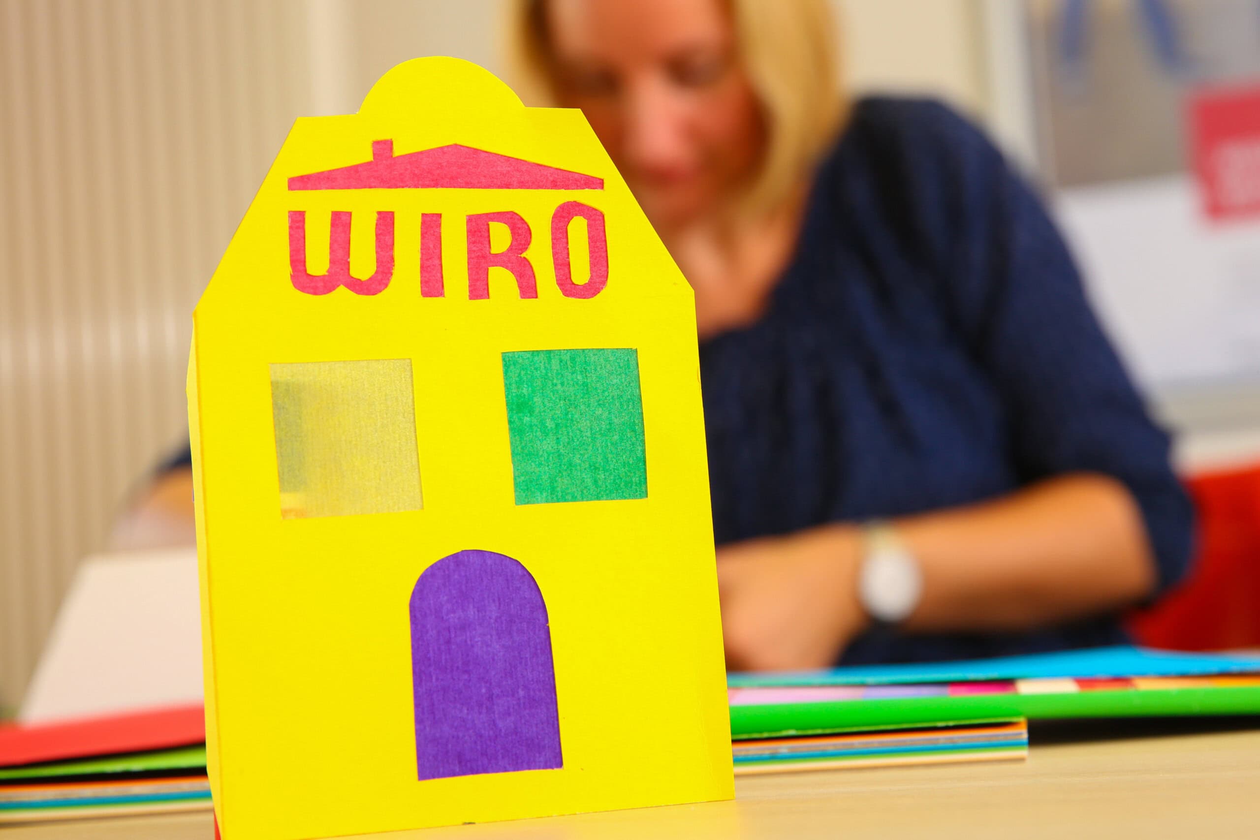 Eine selbst gebastelte gelbe Laterne in Form eines Hauses, mit grünem Fenster und lila Tür sowie der Aufschrift WIRO
