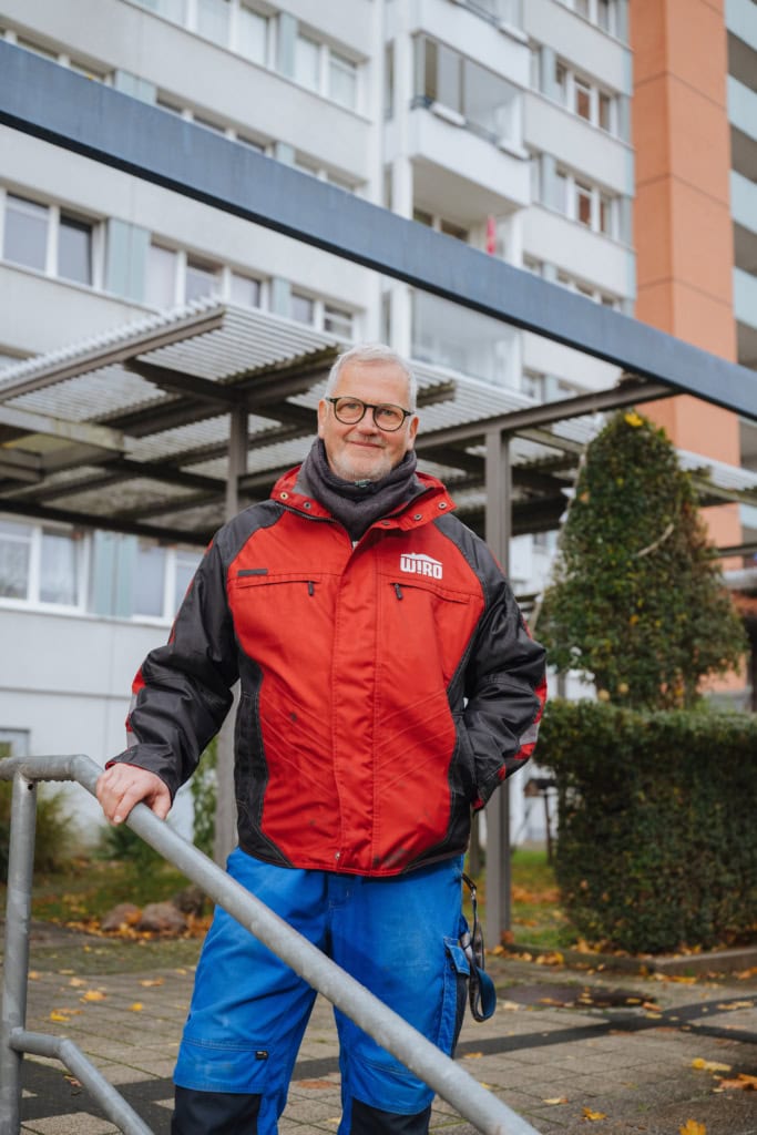 Michael Röllig in roter WIRO-Jacke vor seiner Liguster-Hecke in der Helsinkier Straße.