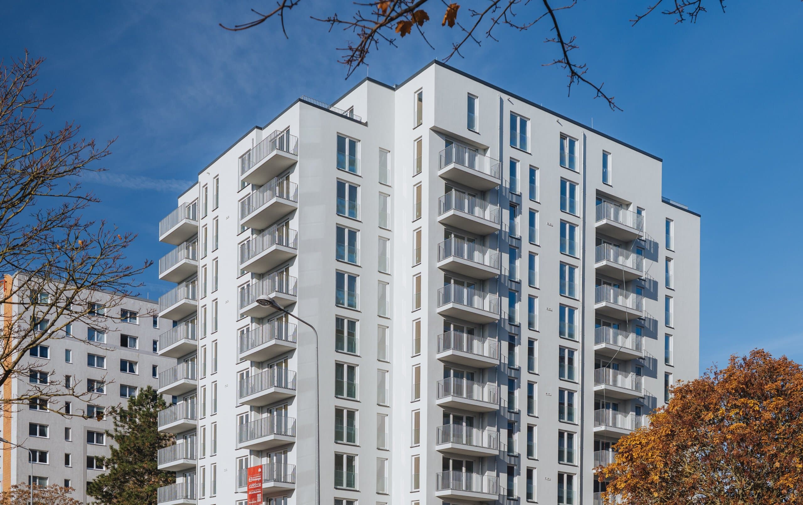 Weißer Neubau in der Warnowallee 23a. Ein modernes Haus mit vielen hohen Fenstern und Balkonen, umsäumt von Bäumen.