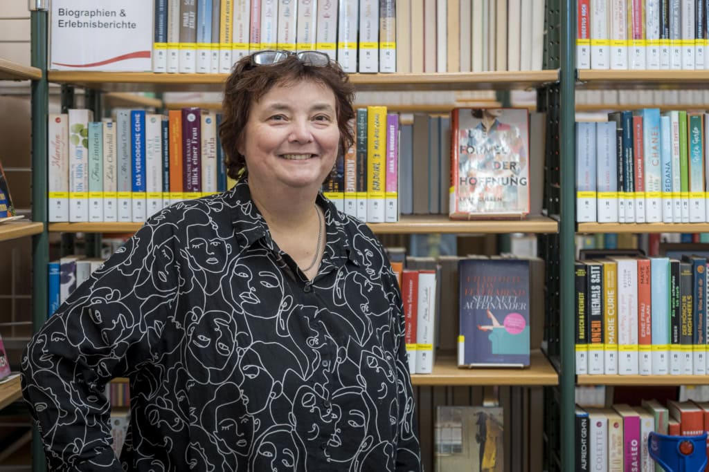 Martina Bade, Direktorin der Stadtbibliothek, braune kurze Haare, Lesebrille in die Haare geschoben, vor einem gut gefüllten Bücherregal.
