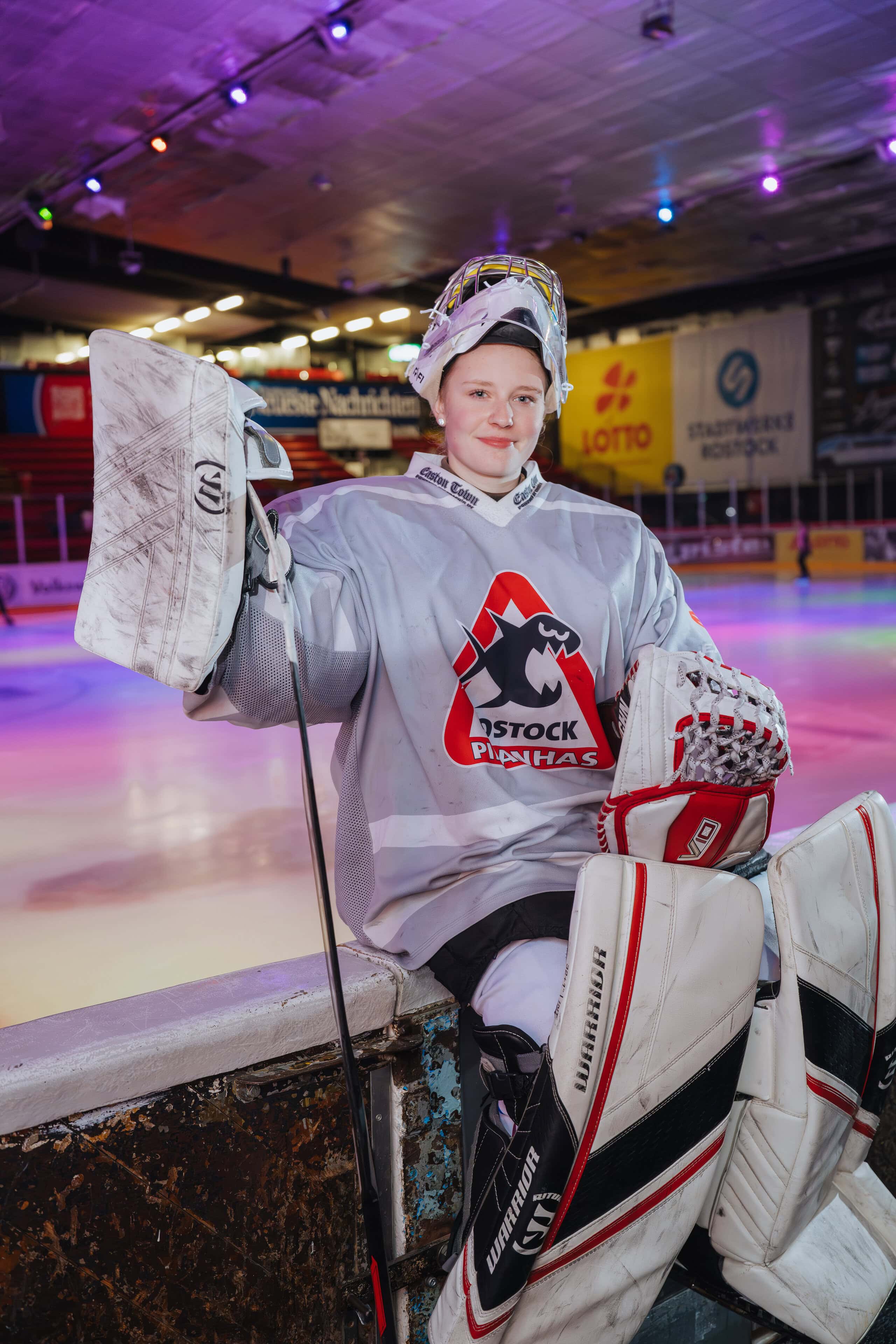 Die 17-jährige Mia Warluks sitzt in Spielermontur, Helm und riesigen Knieschützern auf der Bande neben der eisigen Spielfläche. sie spielt bei den Piranhas Eishockey. Die Rostockerin ist furchtlos und steht sogar im Tor.