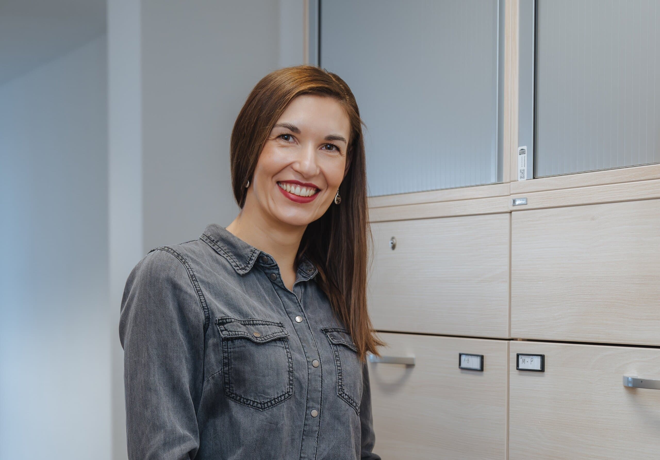 WIRO-Versicherungsfachfrau Diana Lange, lange braune Haare, vorm Aktenschrank in ihrem Büro.