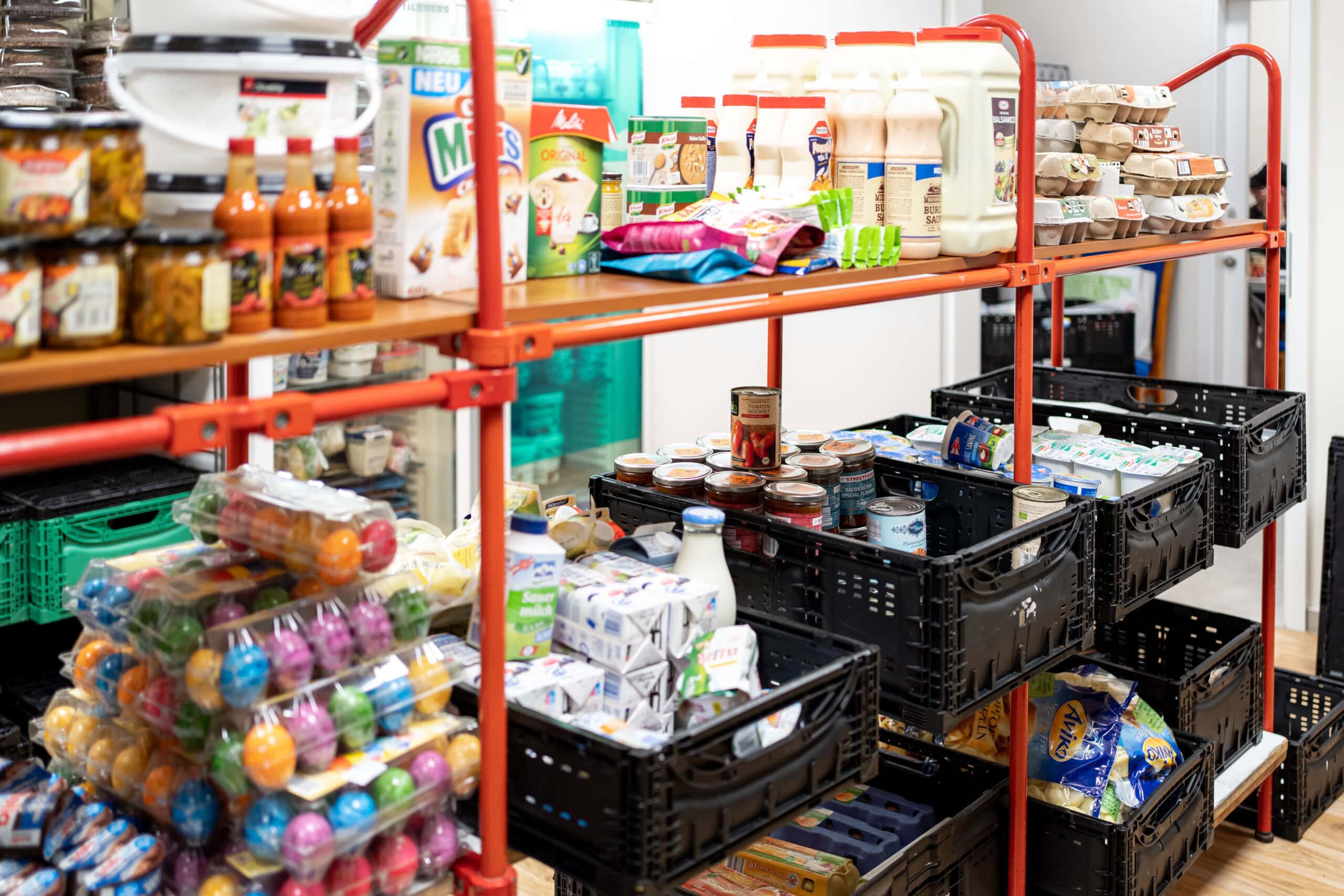 Ein Regal in der Ausgabestelle der Tafel Rostock mit unterschiedlichen Lebensmitteln wie Eier, Milch, Kaffee, Toastbrot und Konserven.