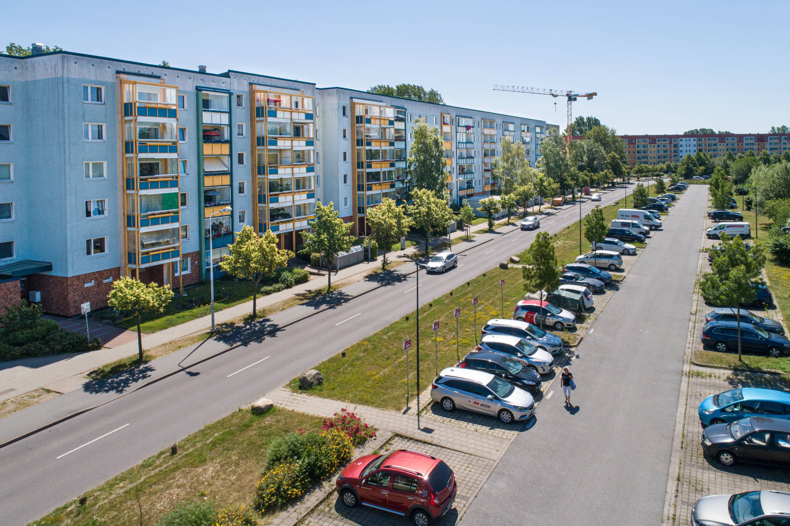 Blick auf eine Straße im Rostocker Stadtteil Groß Klein, links der Straße stehen Mehrfamilienhäuster mit sechs Etagen, rechts der Straße befinden sich Parkplötze für die Mieter