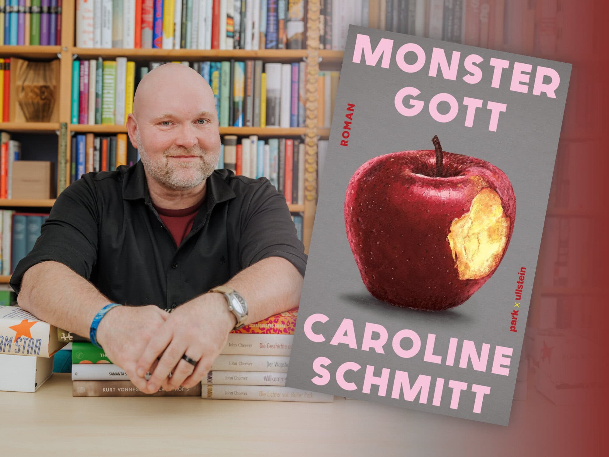 Bookster Andreas Härtel sitzt vor einem großen Bücherregal stützt seine Arme auf Bücherstapel, neben ihm das Titelbild des Romans "Monstergott" von Caroline Schmitt