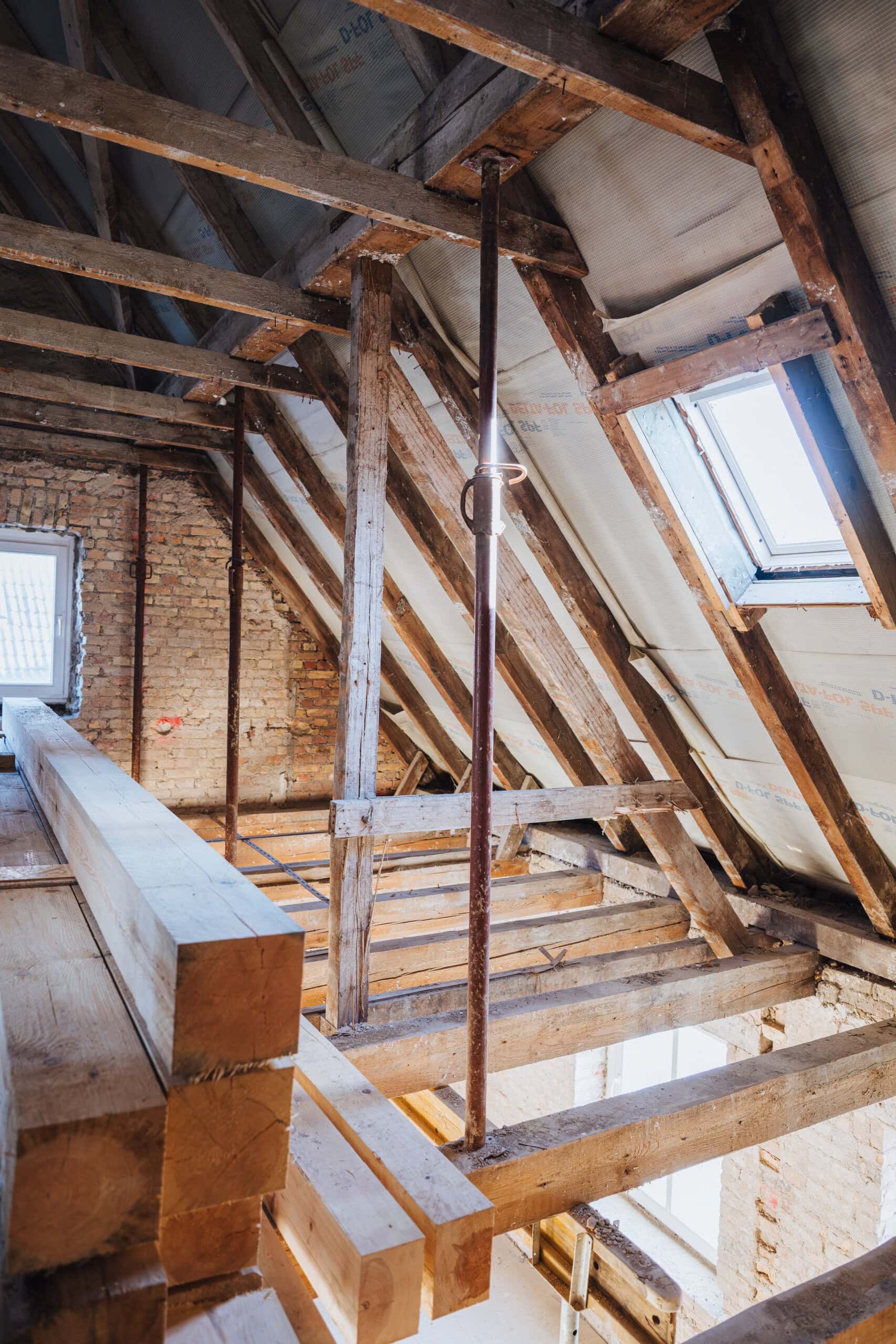 Dachbalken, Steinwände ohne Putz. Durch die Dachfenster scheint Sonne in die Baustelle.