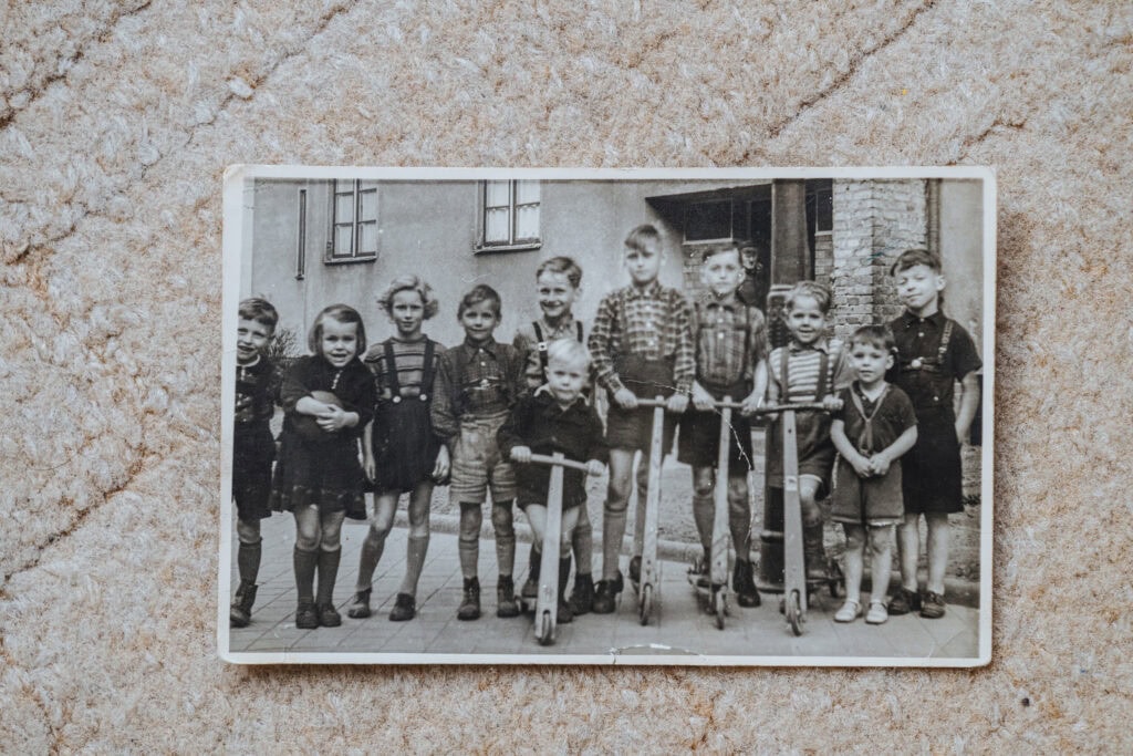Ein altes Schwarz-Weiß-Foto, auf dem eine Truppe Kinder mit Holzrollern in einer Reihe stehen.