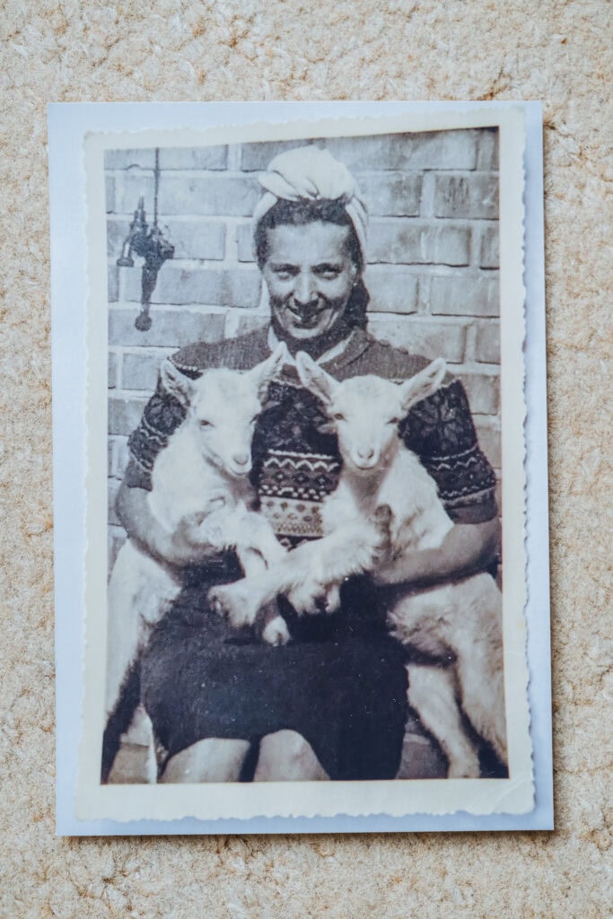 Ein altes privates Schwarz-Weiß-Foto, auf dem eine lächelnde Frau mit zwei jungen Zicklein im Arm zu sehen ist.