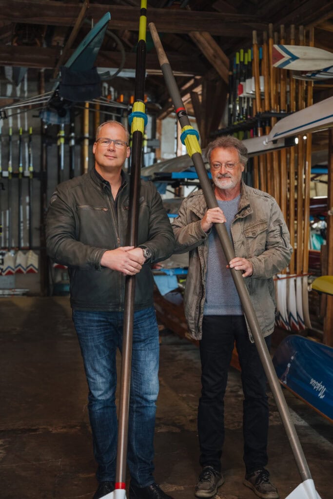Sven Nagel (links) und Ronald Förster in der Rostocker Ruder-Club-Bootshalle am Gehlsdorfer Ufer. Beide Männer halten ein Ruder in der Hand.