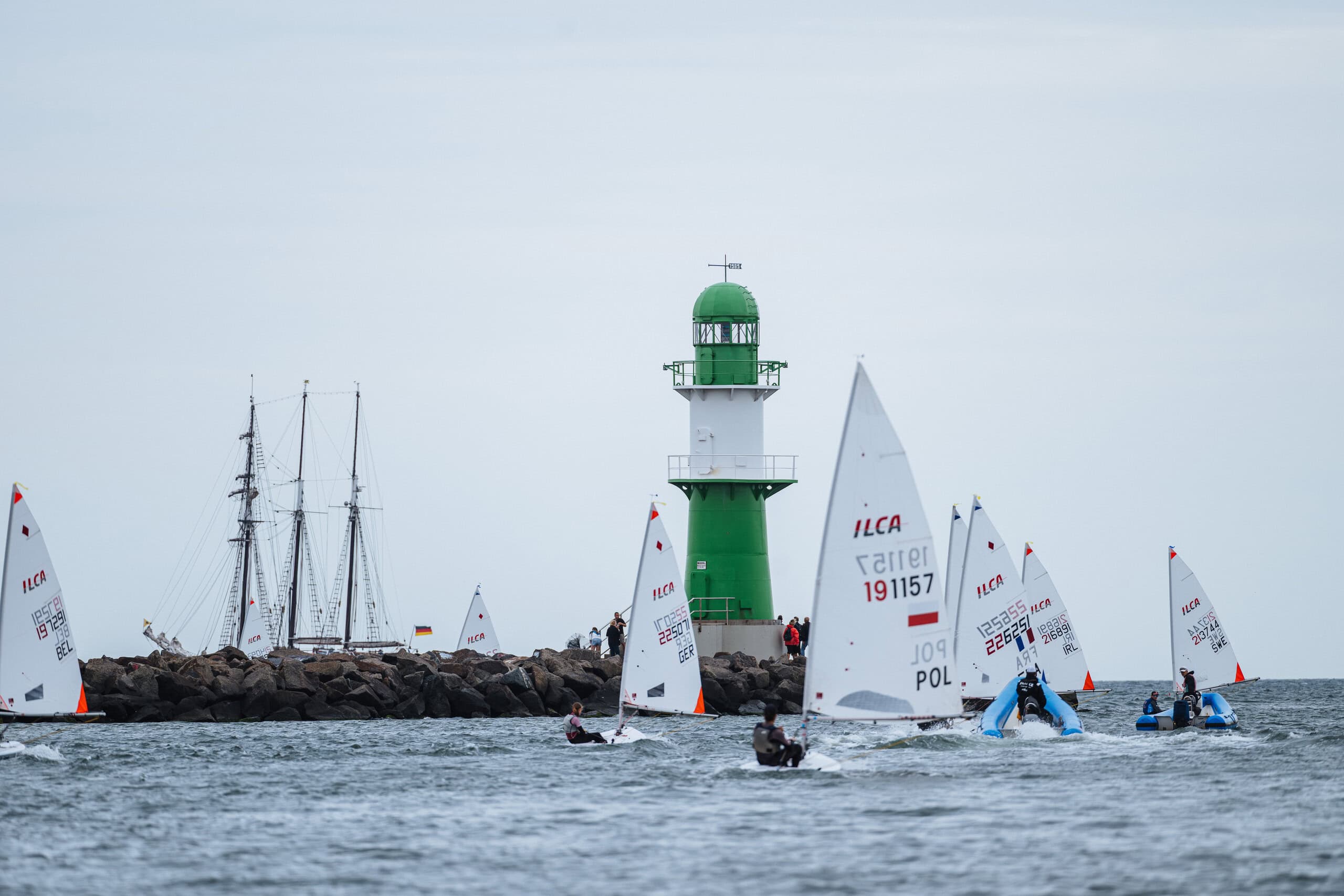 Segelboote auf der Warnemünder Woche kreuzen vor der Mole mit Leuchtturm.